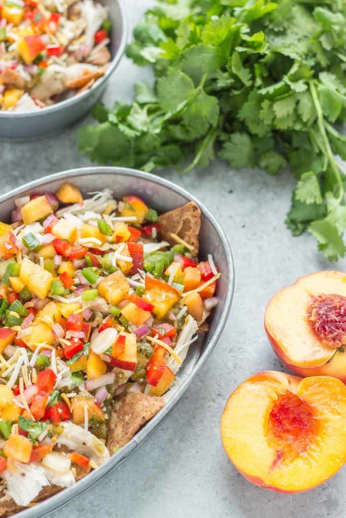 Chicken Nachos with Peach Salsa are bursting with bright summer flavors. Featuring juicy, ripe peaches, fresh chopped veggies and herbs, perfectly cooked chicken and a homemade tomatillo sauce, these nachos will have skipping the taco stand! | Strawberry Blondie Kitchen