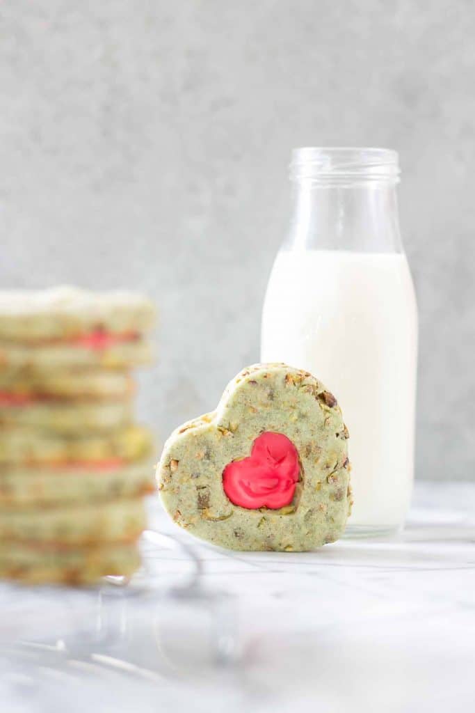 Your heart will grow three sizes with one bite of these Grinch Sandwich Cookies.  Pistachio shortbread cookies, with heart cutouts and red icing pay homage to one of childhood's favorite movies. | Strawberry Blondie Kitchen