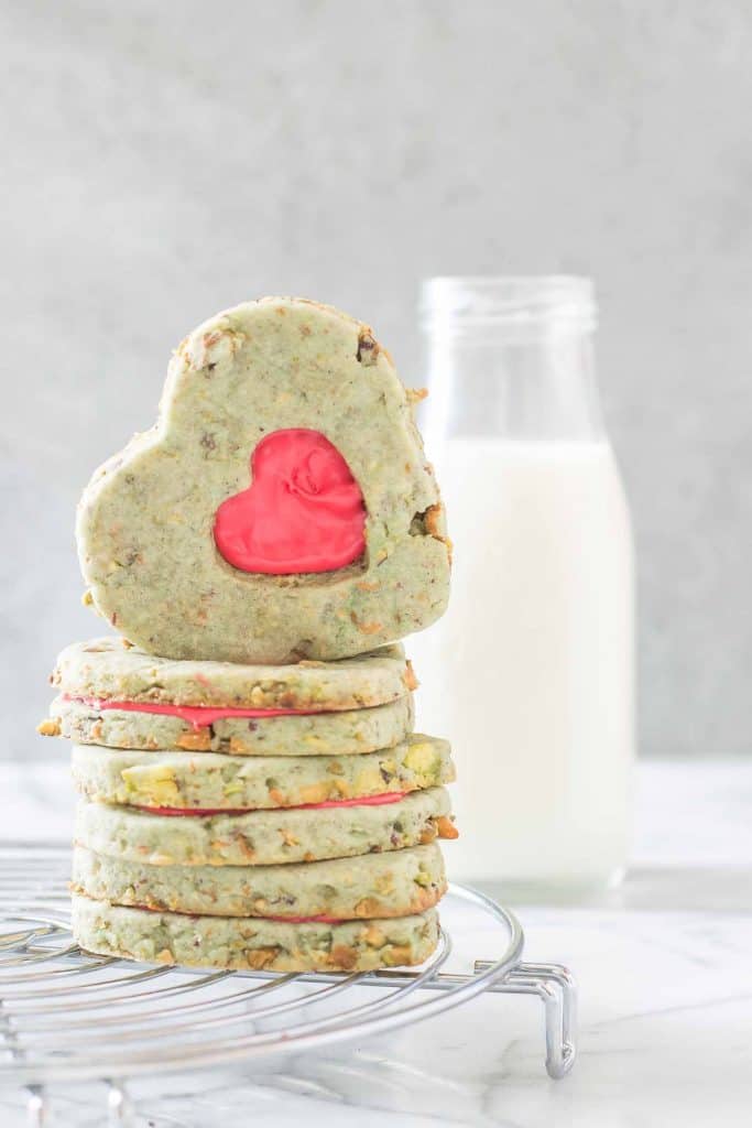 Your heart will grow three sizes with one bite of these Grinch Sandwich Cookies.  Pistachio shortbread cookies, with heart cutouts and red icing pay homage to one of childhood's favorite movies. | Strawberry Blondie Kitchen