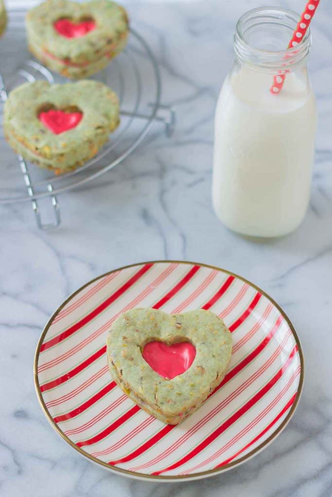 Your heart will grow three sizes with one bite of these Grinch Sandwich Cookies.  Pistachio shortbread cookies, with heart cutouts and red icing pay homage to one of childhood's favorite movies. | Strawberry Blondie Kitchen