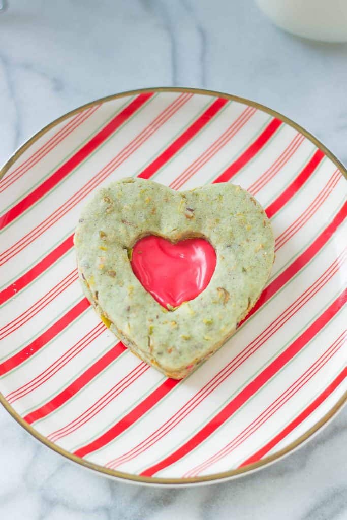 Your heart will grow three sizes with one bite of these Grinch Sandwich Cookies.  Pistachio shortbread cookies, with heart cutouts and red icing pay homage to one of childhood's favorite movies. | Strawberry Blondie Kitchen