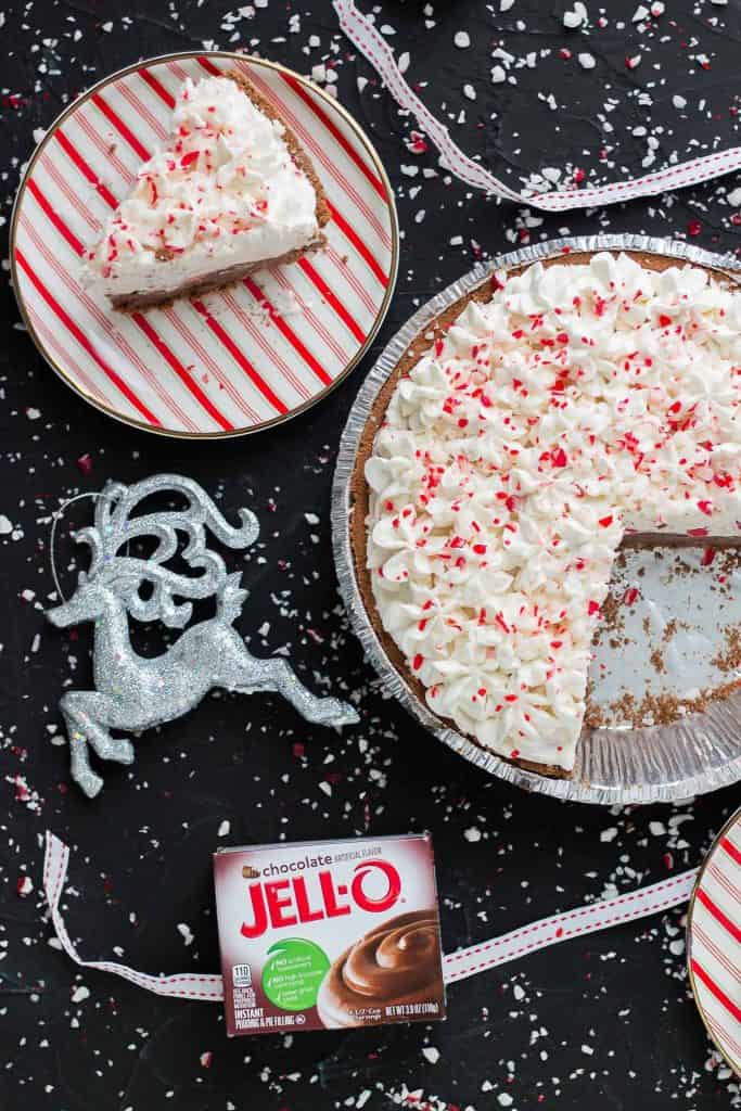 A slice of no bake candy cane pie with the whole pie beside it and a box of chocolate JELL-O