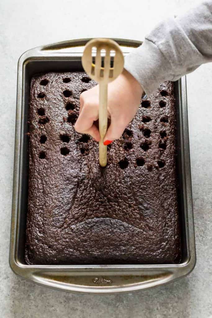 Use the end of a wooden spoon to poke holes into homemade chocolate cake so you can pour the liquid in