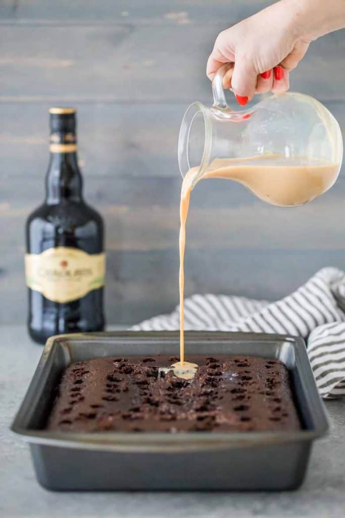 Pouring Baileys Irish Cream into homemade chocolate poke cake