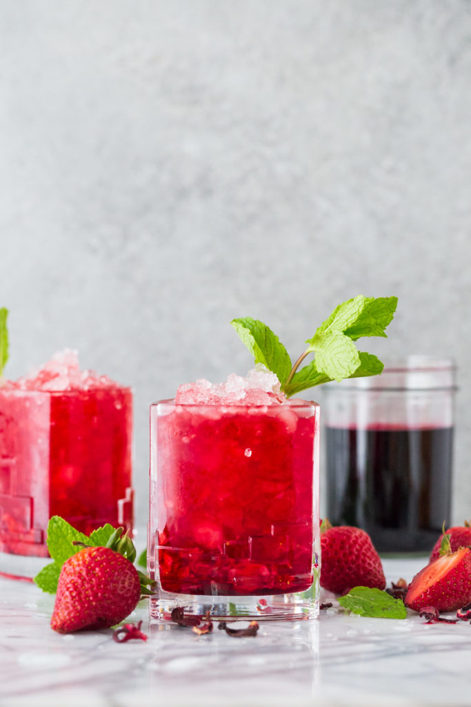 Bright red strawberry cocktail infused with hibiscus tea in a glass garnished with mint 