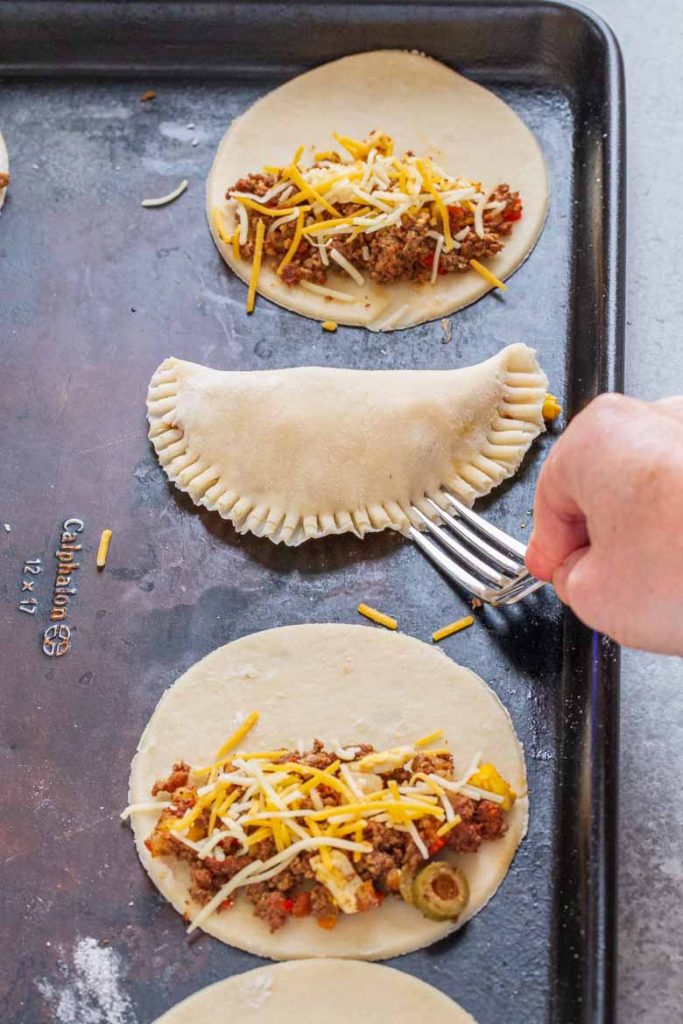 Using the tines of a fork, crimp edges all around empanada filling to close the pocket