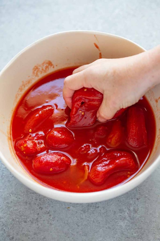 Place San Marzano tomatoes into a bowl and crush with your hands