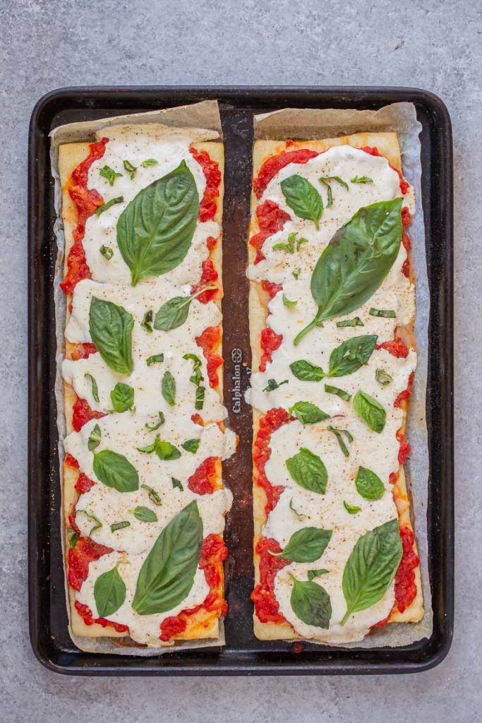 Top margherita flatbread with fresh basil leaves