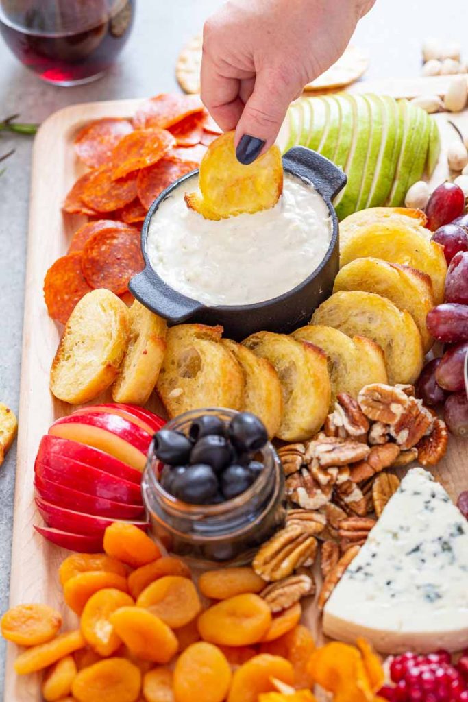 Dipping a garlic bread toast into Blue Cheese Fondue Charcuterie Board 