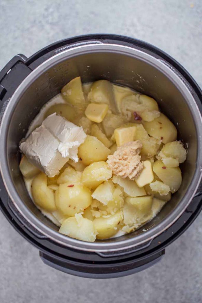Instant pot full of quartered red potaotes, cream cheese, milk, horseradish and butter for instant pot horseradish mashed potatoes