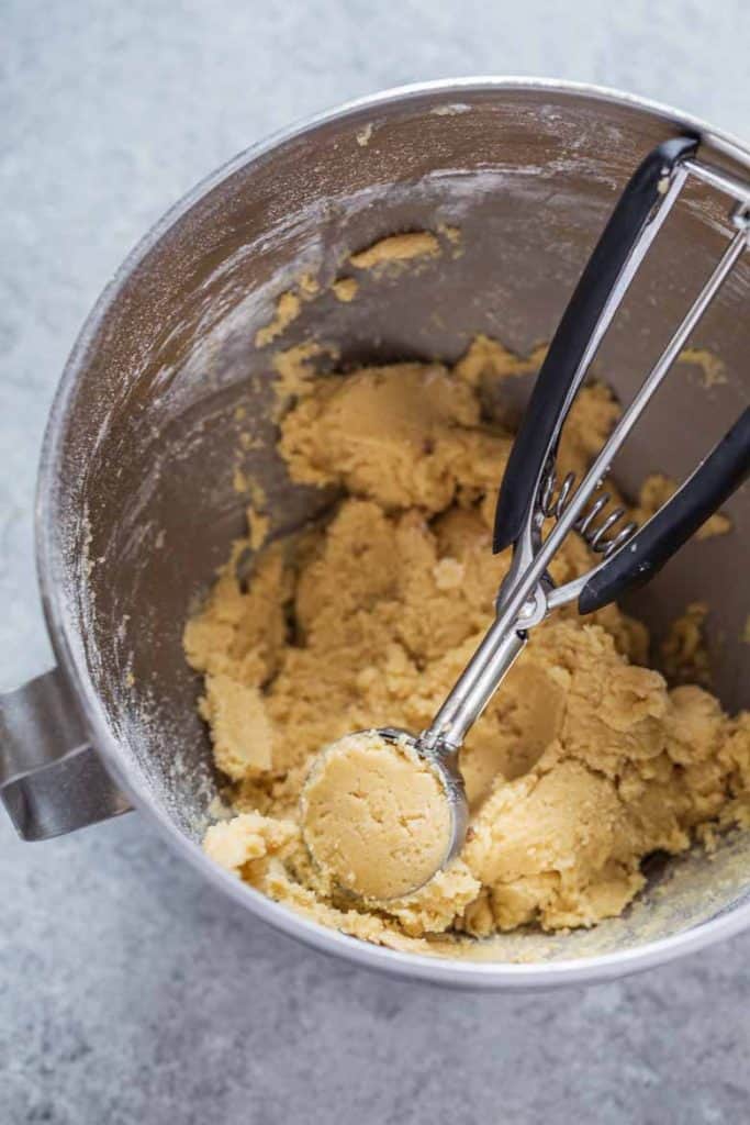 Snickerdoodle cookie dough in a mixing bowl with a cookie scoop