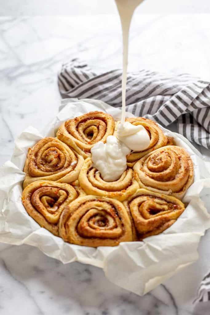 Drizzle of thick cream cheese icing on top of carrot cake cinnamon rolls