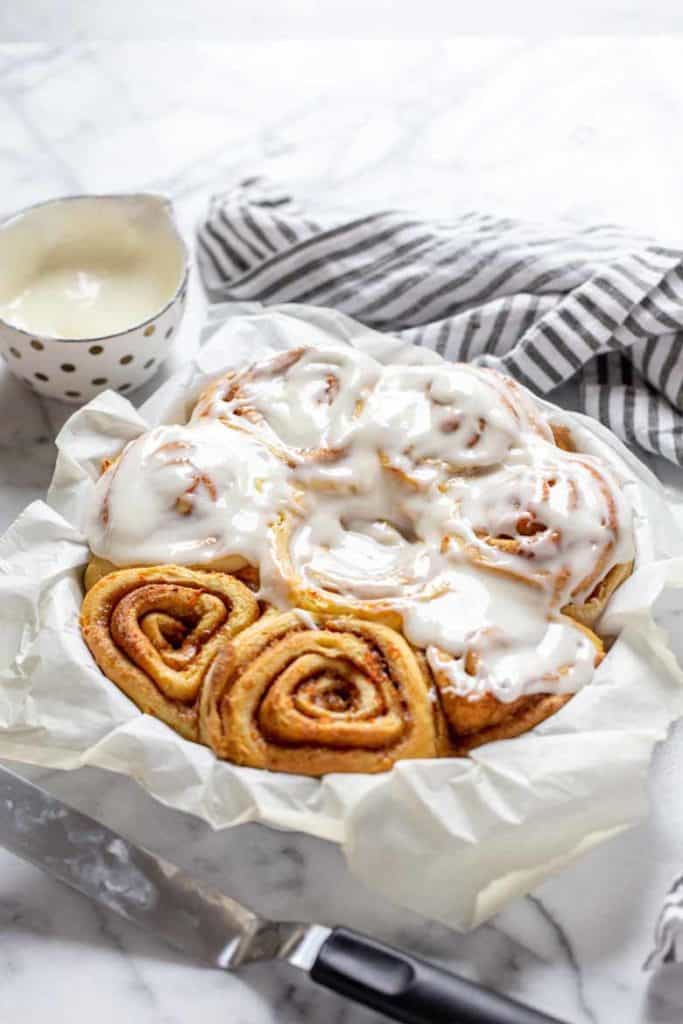 carrot cake cinnamon rolls in a pan with half drizzled in cream cheese icing