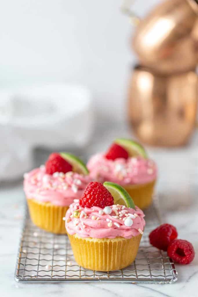 3 Raspberry Moscow Mule Cupcakes lined up with fresh raspberries