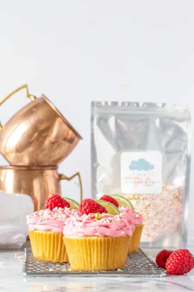 Raspberry Moscow Mule Cupcakes with copper mugs and sprinkles in the background