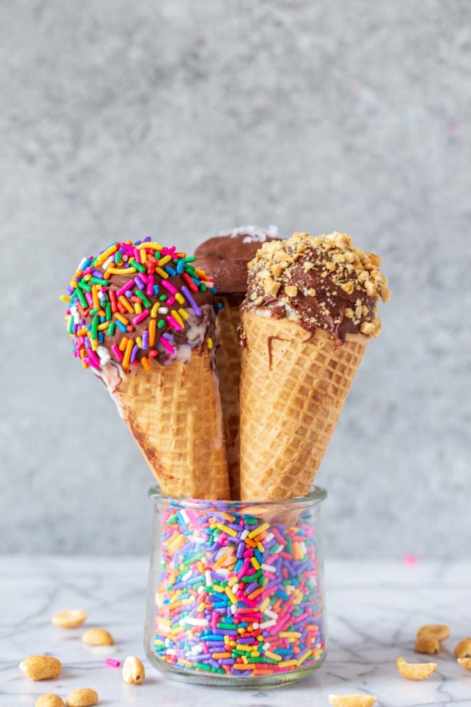 three homemade dipped drumstick ice cream cones styled in a glass jar with colorful sprinkles