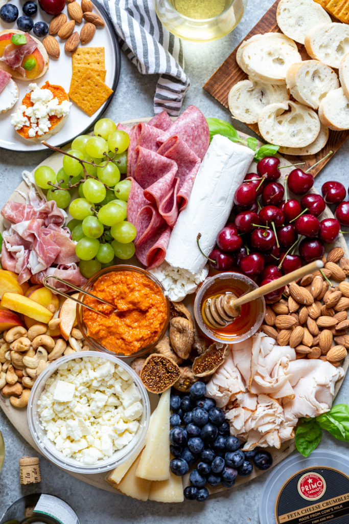 close up shot of meat and cheese board filled with seasonal fruit, nuts, spreads and honey