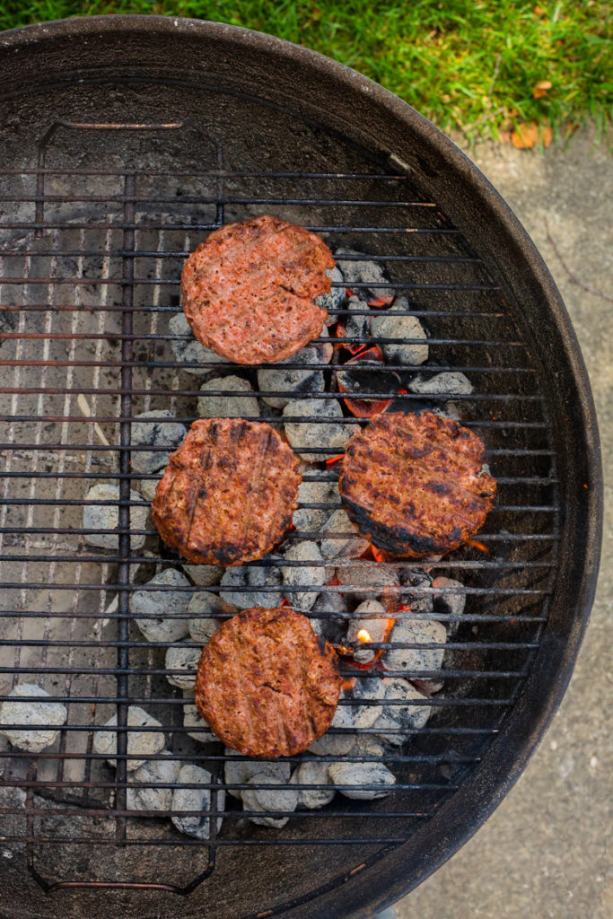 Beyond Meat plant based burger patties being cooked on an outdoor charcoal grill