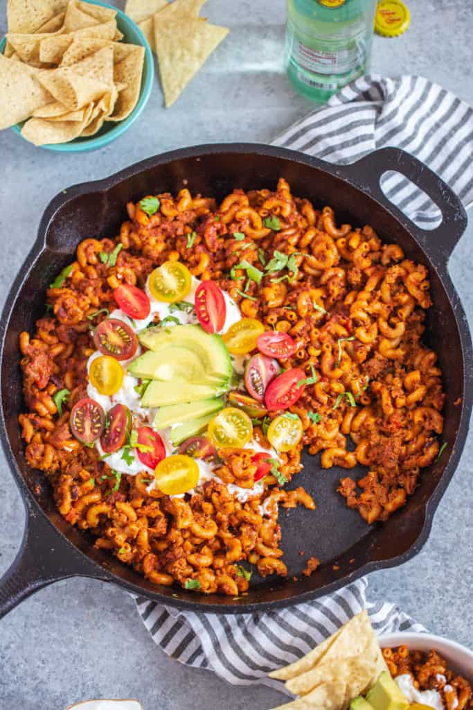 Healthier One Pan Taco Pasta in cast iron pan topped with sour cream, tomatoes and avocado