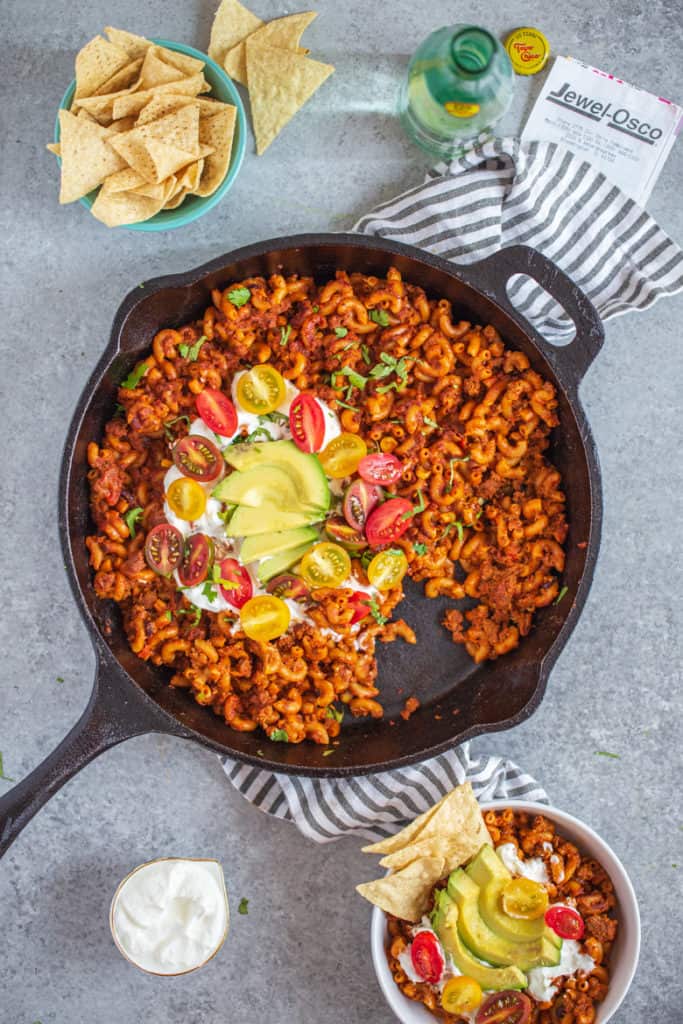 Healthier One Pan Taco Pasta in cast iron pan with sour cream, tomatoes and avocado with a single serving bowl 