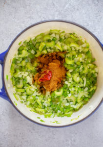 green bell pepper, onion, celery and garlic with tomato paste and cajun seasoning in a pot.