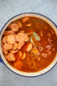 green bell pepper, onion, celery, garlic, tomato paste, cajun seasoning, andouille sausage and red beans in a pot for red beans and rice.