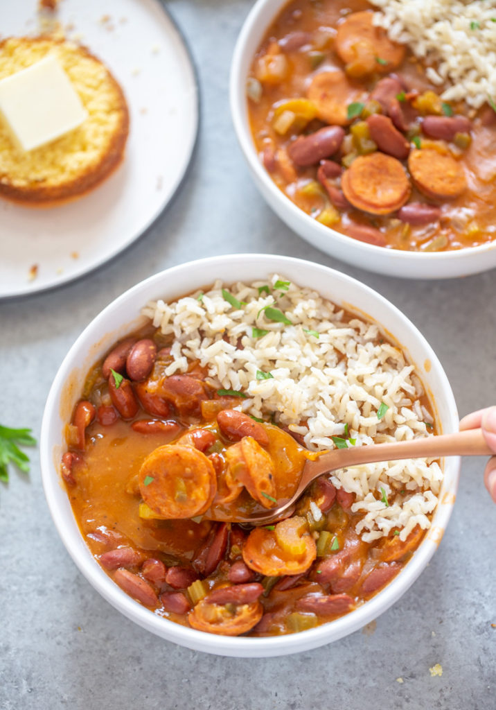 close up image of sausages on spoon from bowl of red beans and rice