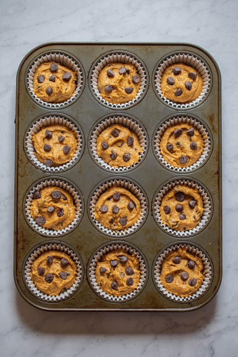Place a few extra chocolate chips on top of pumpkin muffin batter in muffin tin.