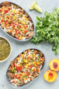 Chicken Nachos with Peach Salsa are bursting with bright summer flavors. Featuring juicy, ripe peaches, fresh chopped veggies and herbs, perfectly cooked chicken and a homemade tomatillo sauce, these nachos will have skipping the taco stand! | Strawberry Blondie Kitchen