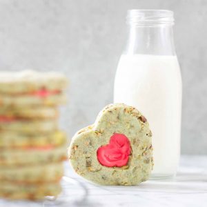 Your heart will grow three sizes with one bite of these Grinch Sandwich Cookies.  Pistachio shortbread cookies, with heart cutouts and red icing pay homage to one of childhood's favorite movies. | Strawberry Blondie Kitchen