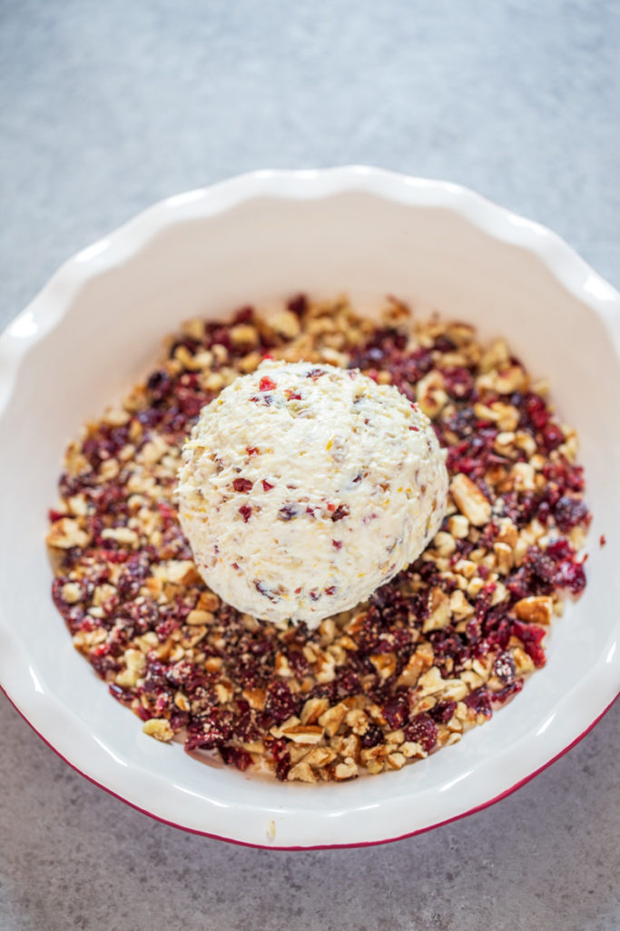 Spread additional crushed pecans (¼ cup) and dried cranberries (¼ cup) on the counter; roll ball in them until covered.