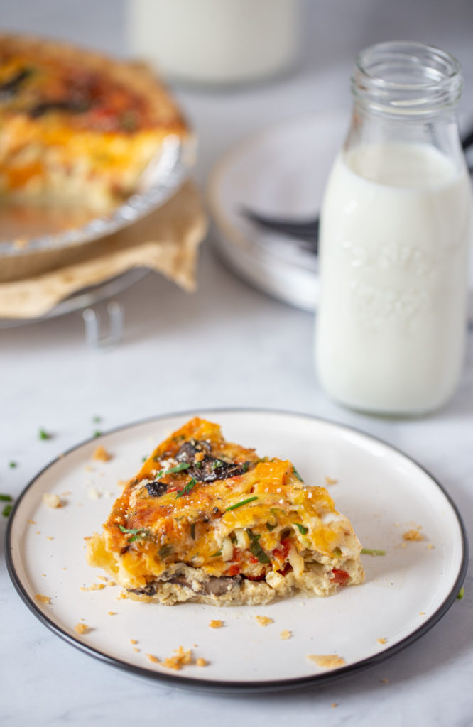 Side shot of a single slice of vegetable quiche with a bottle of milk