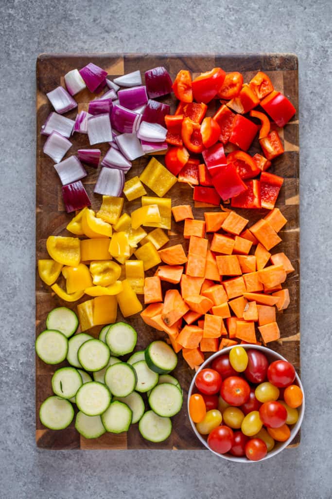 Cutting board filled with chopped bell peppers, onions, zucchini and cherry tomatoes.