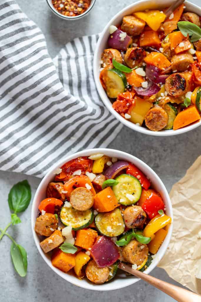 Bowls filled with oven roasted vegetables and chicken sausages, topped with fresh basil and parmesan cheese