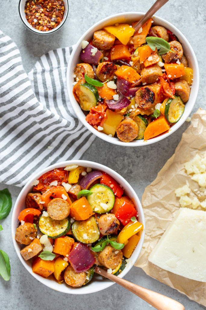 Bowls filled with oven roasted vegetables and chicken sausages, topped with fresh basil and parmesan cheese