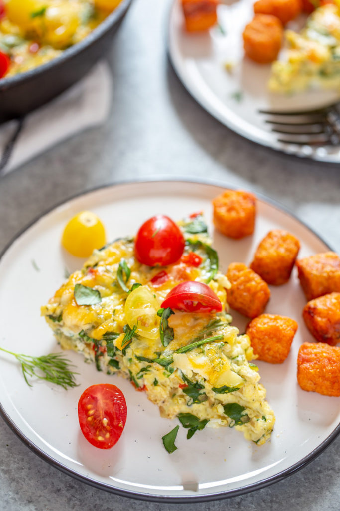 Close up Garden Herb Frittata slice with cherry tomatoes and sweet potato tots.