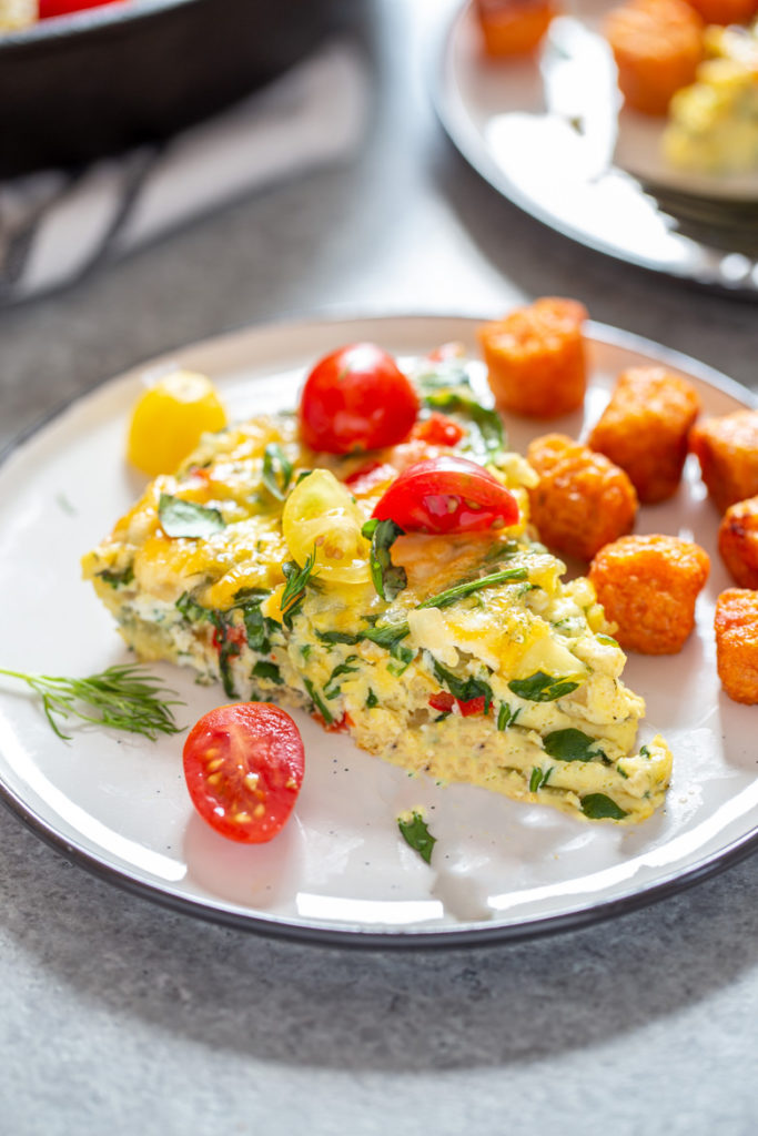 Close up photography shot of slice of Garden Herb Frittata on a plate with sweet potato tots and cherry tomatoes