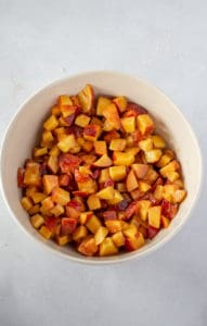Bowl of chopped peaches covered in cornstarch, spices, brown sugar and lemon for peach cobbler bars